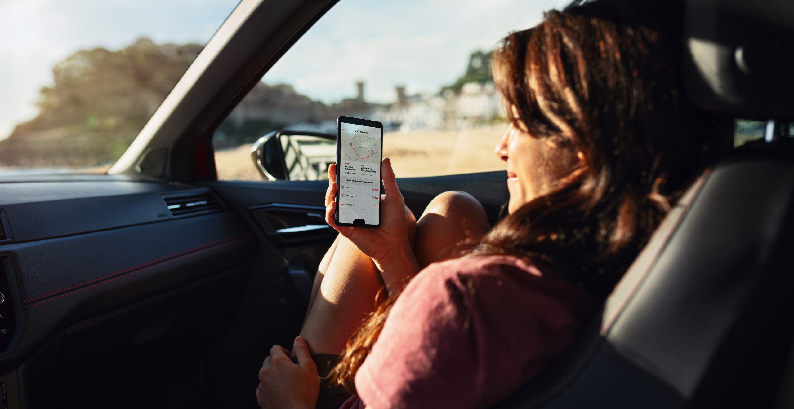 Frau sitzt in einem SEAT Fahrzeug mit ihrem Smartphone in der Hand.