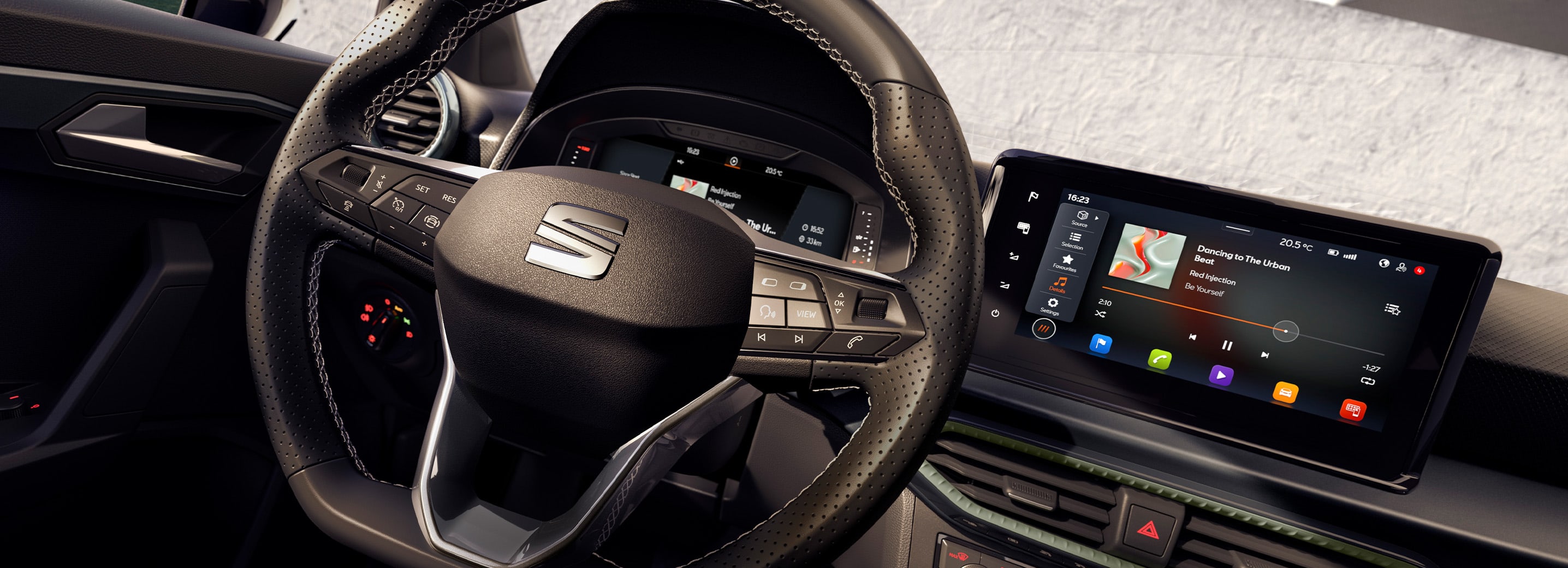 Lenkrad und Armaturenbrett eines SEAT-Fahrzeugs, Modell Arona. Sichtbar sind ein Display mit Musikwiedergabe und digitale Anzeigen. Schaltknauf und diverse Bedienelemente für Klimaanlage und Infotainment im Vordergrund