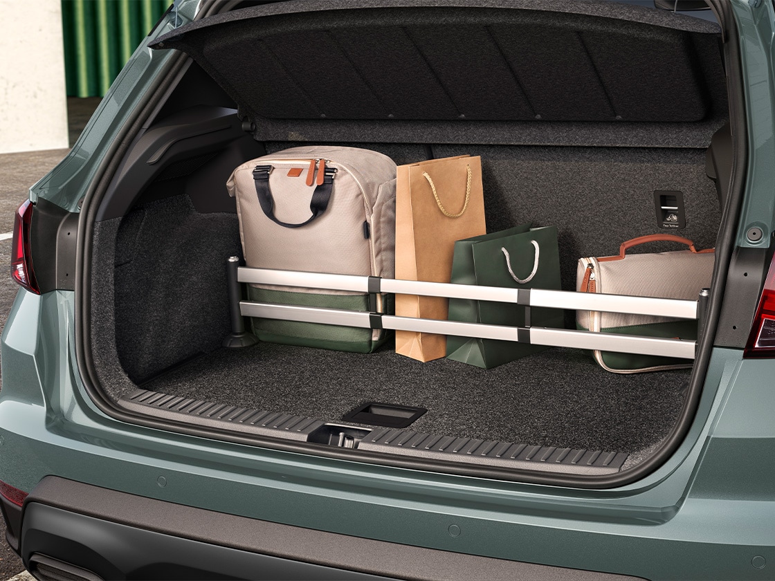 Geöffneter Kofferraum eines SEAT Arona, gefüllt mit einer großen Tasche, zwei Papier-Einkaufstüten und einer kleinen Tasche, die durch eine verstellbare Stange gesichert sind. Der Fahrzeugaußenlack ist grün.