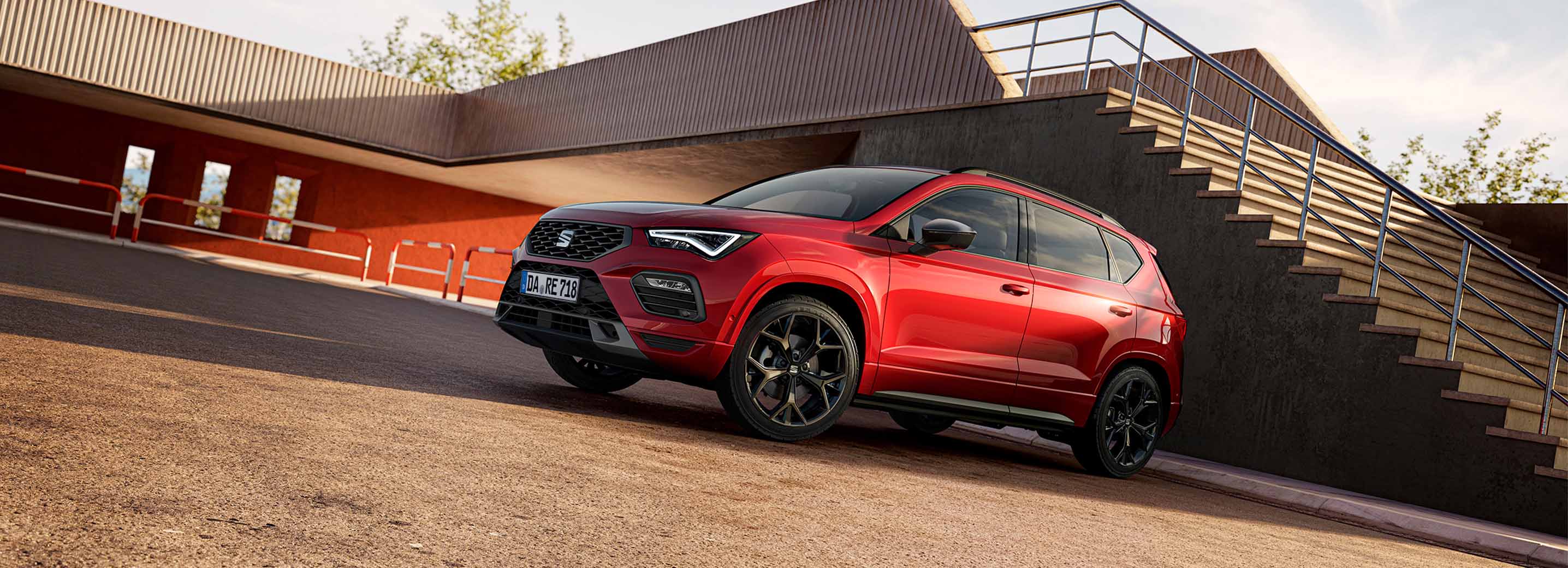 Roter SEAT Ateca in schräger Front-Seitenansicht vor moderner Architektur mit Treppe