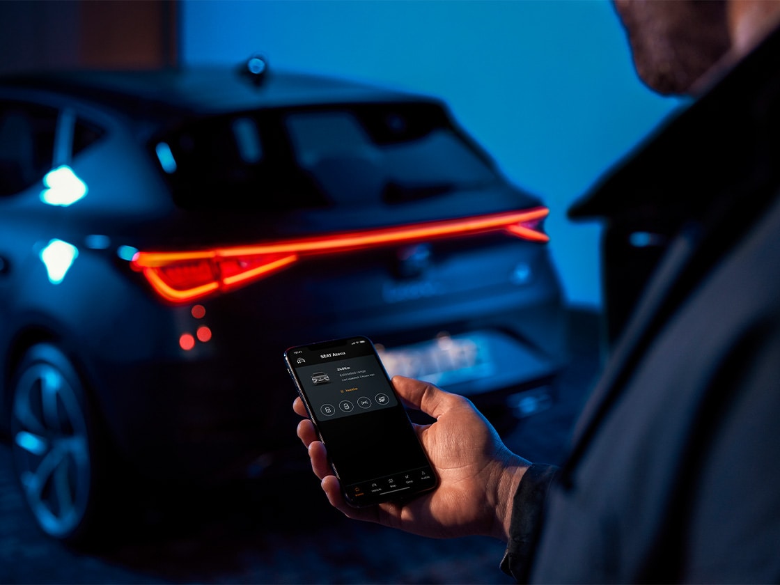 Person hält ein Smartphone mit Fernzugriff-Funktionen für einen SEAT Ateca, Fahrzeug im Hintergrund
