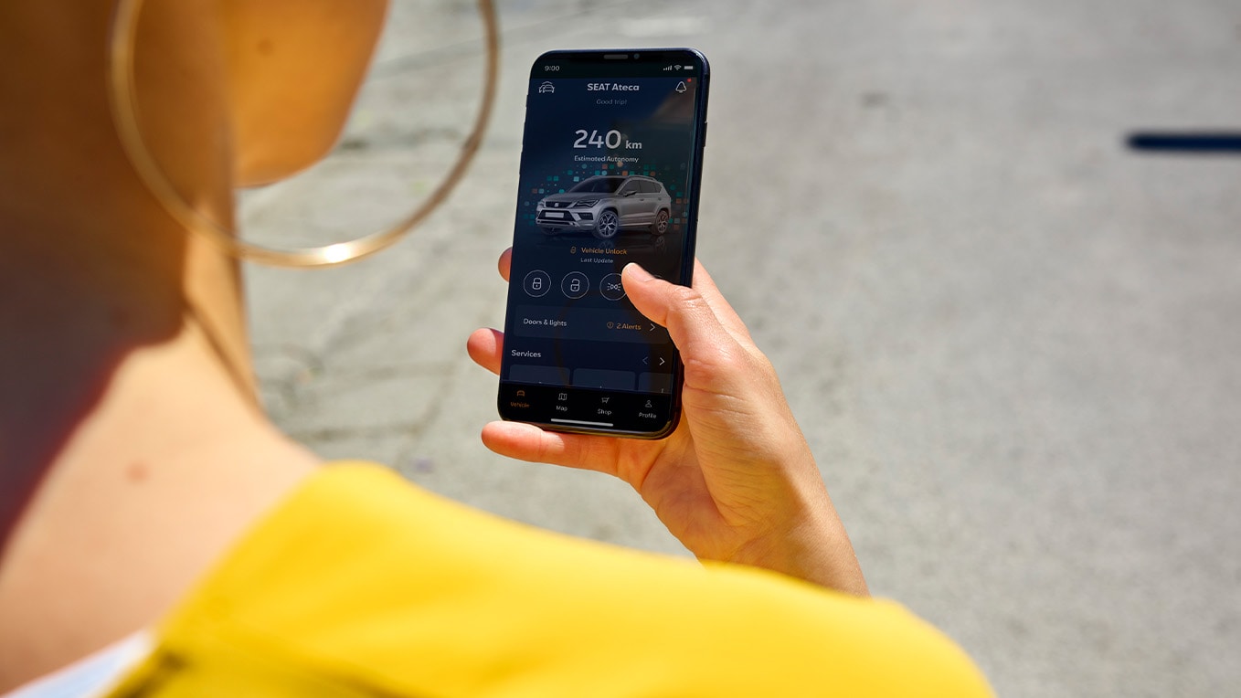 Person hält ein Smartphone mit der SEAT Connect App zur Fernsteuerung eines SEAT Ateca, Anzeige von Fahrzeugstatus und Reichweite