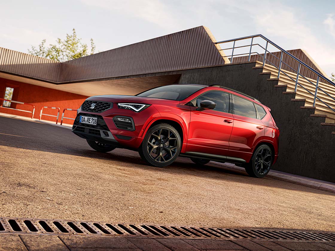 Roter SEAT Ateca in schräger Front-Seitenansicht vor moderner Architektur mit Treppe