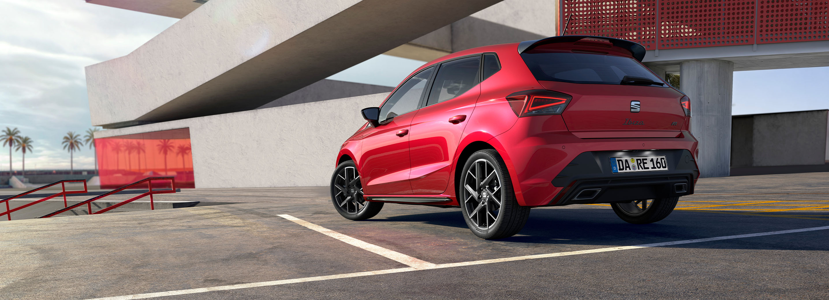 Roter SEAT Ibiza von hinten auf einem Parkplatz, modernes Gebäude im Hintergrund. Nummernschild mit deutscher Kennung.  Parkstreifen und rote Geländer im Vordergrund