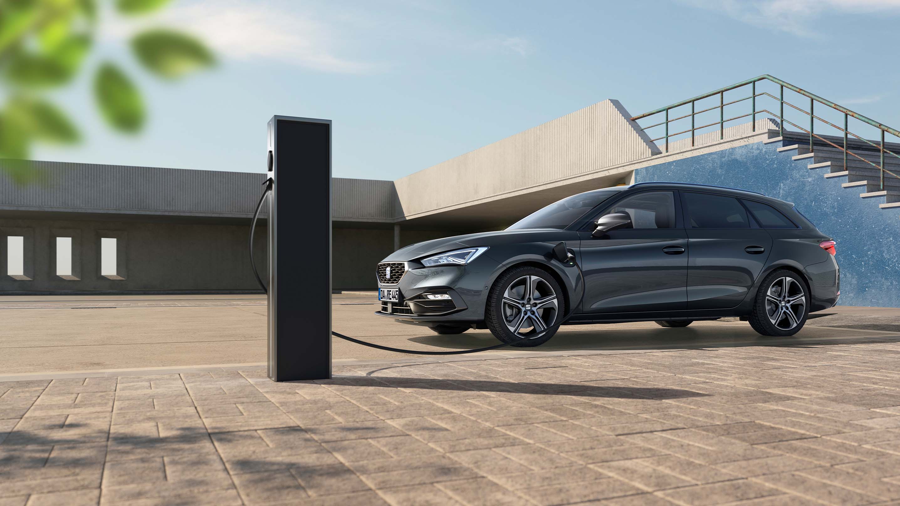 Seitenansicht eines Magnetic Tech SEAT Leon Sportstourer, geparkt vor einer dunkelblauen Wand und einer Treppe, die aufgeladen wird.
