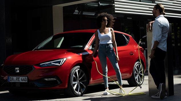 Hybrid car seat leon in red and driver, rear view low angle, brick wall and blue sky