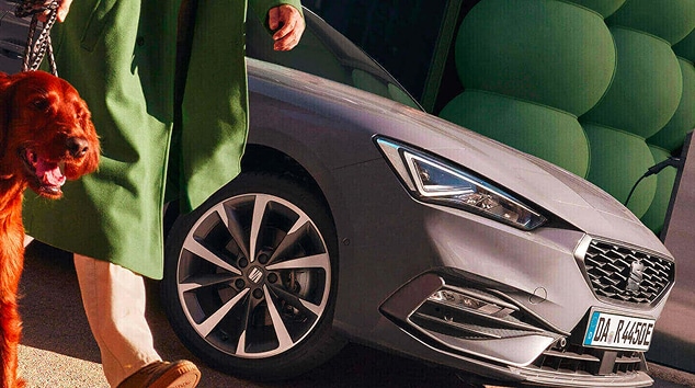 Hybrid car seat leon charging at a public charging station on a rainy street at night, highlighting the advantages of hybrid vehicles