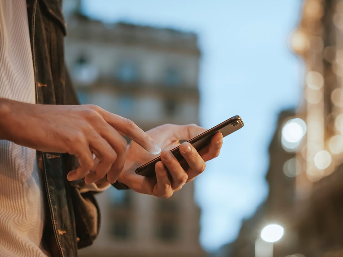 Ein Mann blickt auf sein Smartphone, während er mit der App sein Fahrzeug entriegelt. 