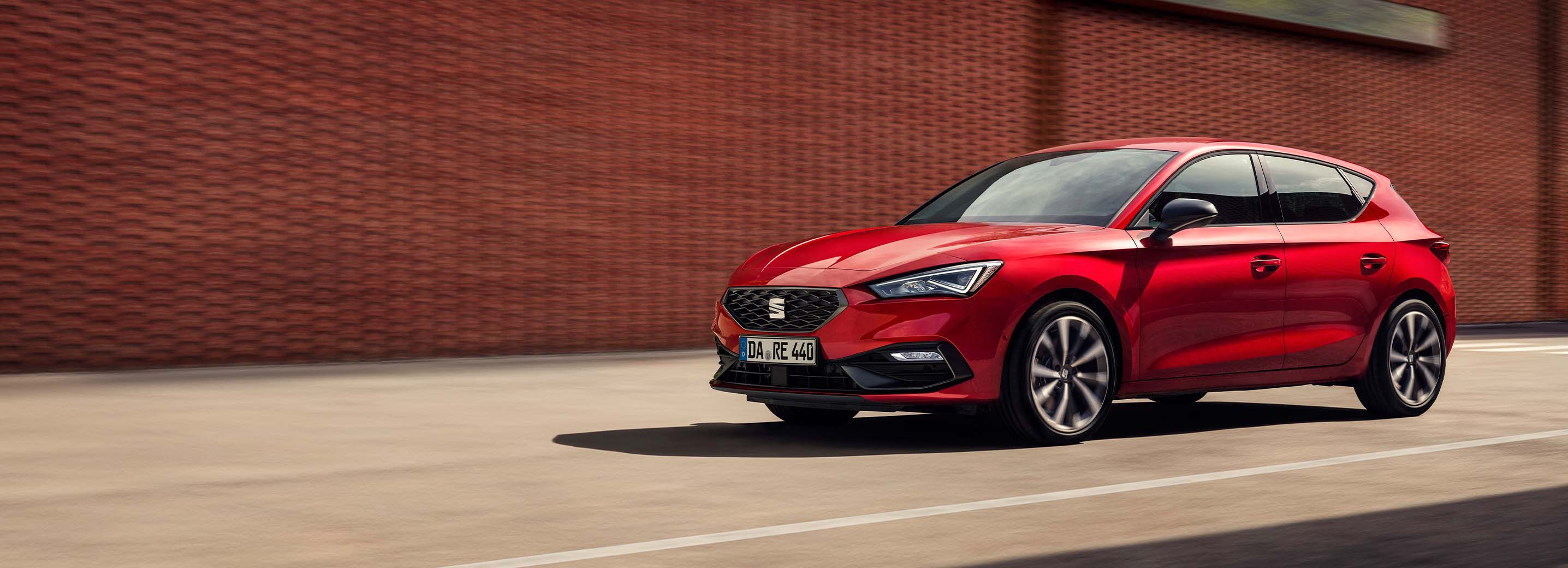 Seitenansicht eines fahrenden SEAT Leon e-HYBRIDs vor einer Backsteinwand.