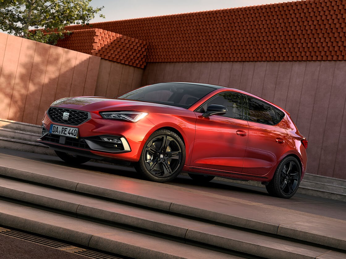 Seitenansicht des roten SEAT Leon FR Black Edition vor einem modernen Gebäude. 