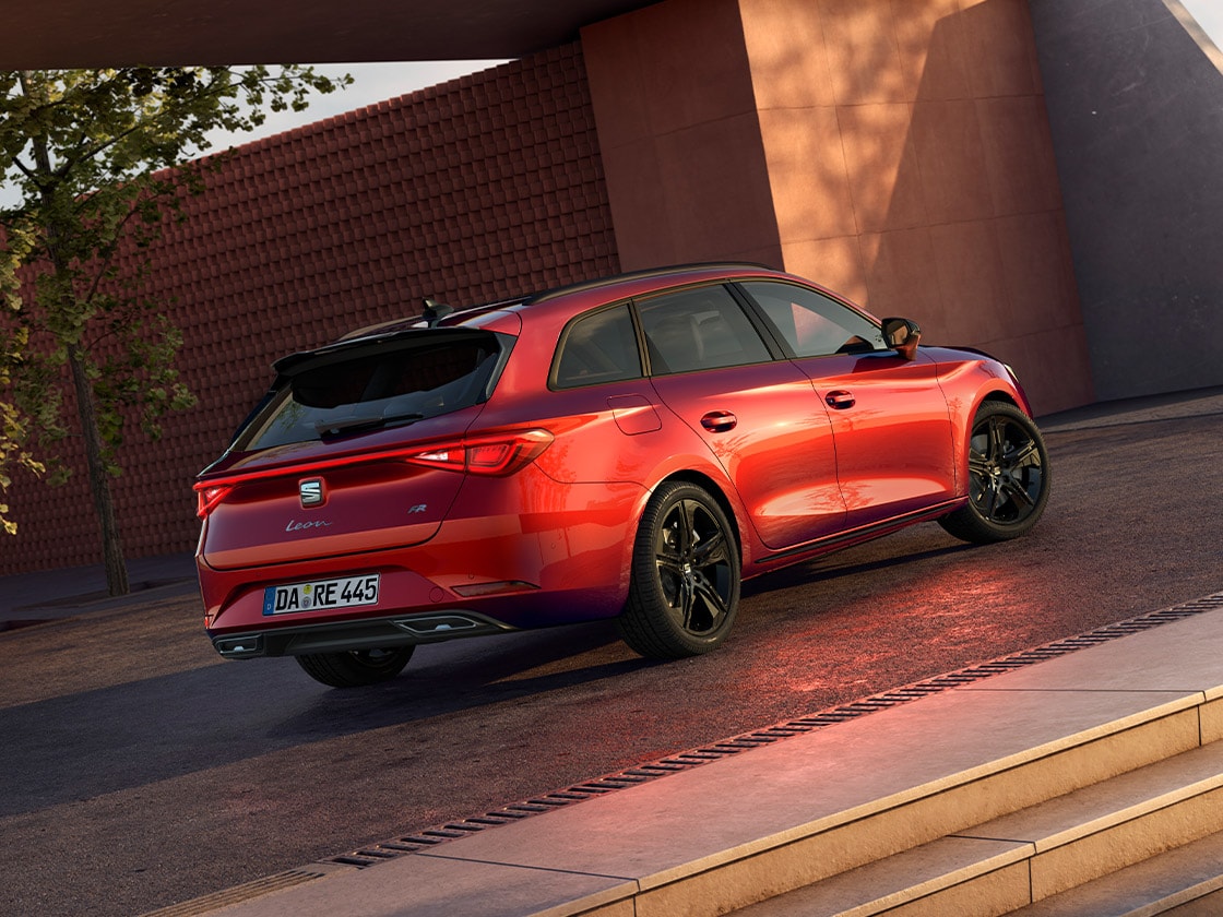 Seitenansicht des roten SEAT Leon Sportstourer FR Black Edition vor einem modernen Gebäude. 